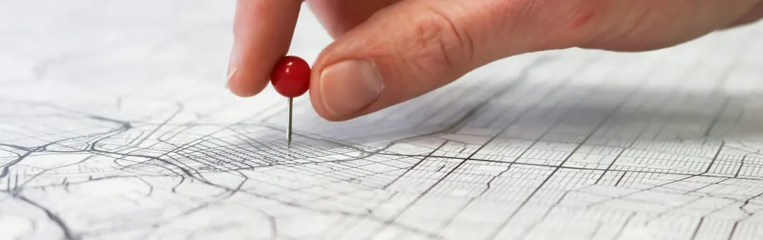 Hand pressing a red pin into a printed street map to mark a location