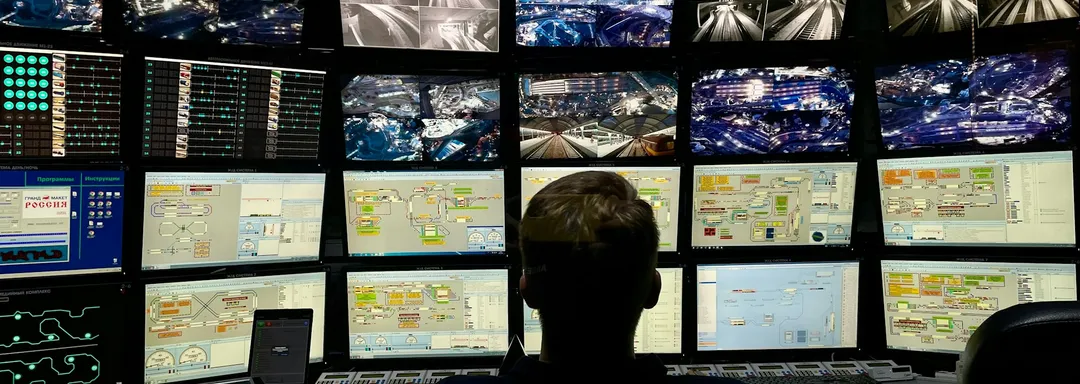 Security officer monitoring a wall of CCTV screens in a control room, watching for BOLO subjects.