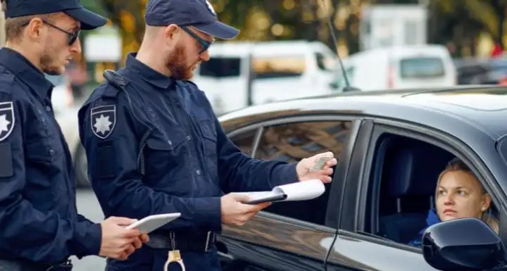 Two uniformed officers beside a car, one returning documents to the driver through the window