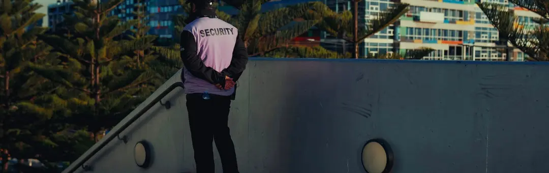 Security guard in a SECURITY vest keeping watch from a concrete walkway above city buildings