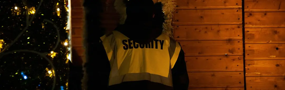 Security officer in a high visibility SECURITY vest on duty at night beside a lit tree