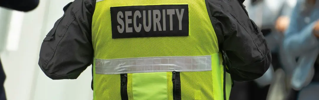 Security officer in a marked vest and duty belt patrolling a street